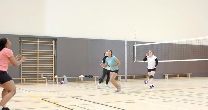Diverse female volleyball teammates on court reacting to ball, setter catching, pushing for spike