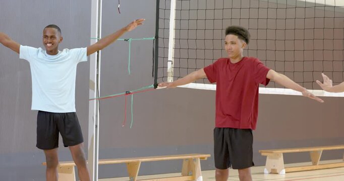 African American male volleyball teammates starting warm-up holding T-pose at gym net for practice