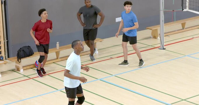 Male team tracking volleyball from right at gym, white tee setter raising performing overhead set
