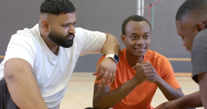 Break from game driving diverse male friends discussing tactics on sports court using smartwatch