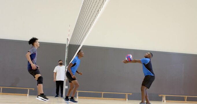 Diverse teammates reacting to incoming ball at net, blocking and bumping in gym to continue rally