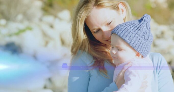 Mother holding infant cradling for health while baby turning toward off-frame stimulus lens flare