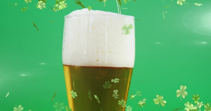 Tall beer glass filling as narrow stream starting to pour, foam rising, clovers drifting for promo