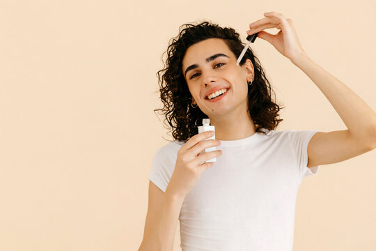 Happy queer man applying face serum with pipette
