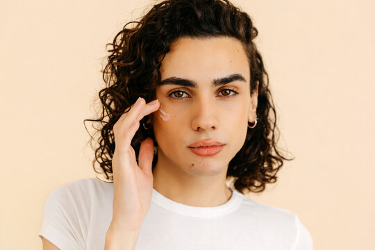 Queer  man applying moisturizer on face 