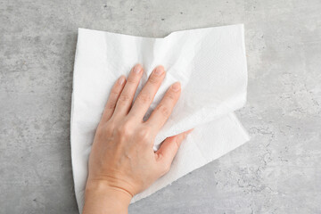 Woman wiping grey textured surface with paper towel, top view