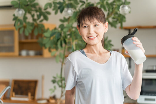 Asian woman drinking protein and EAA after training in the living room at home