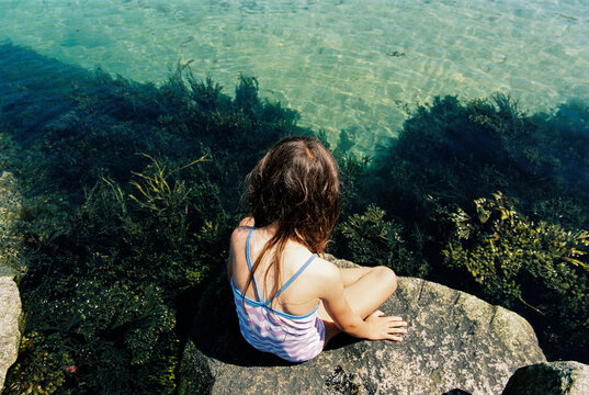 Child sits on a rock by the ocean
