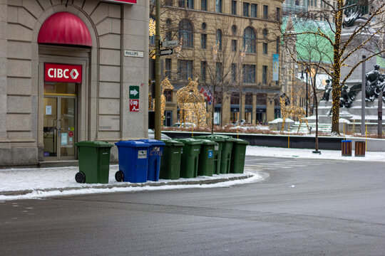 MONTREAL, CANADA, 23 December 2025 : Winter city street scene, recycling bins, holiday decorations, urban landscape, CIBC building, snowy sidewalk, downtown intersection