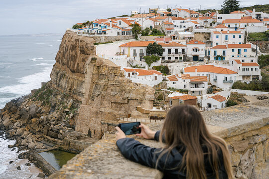 Young woman taking pictures of cliff town on Atlantic Ocean