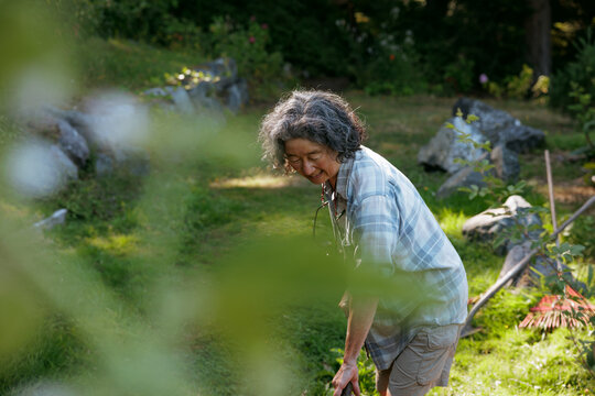 Woman gardening outdoors in a nature-filled backyard with rake