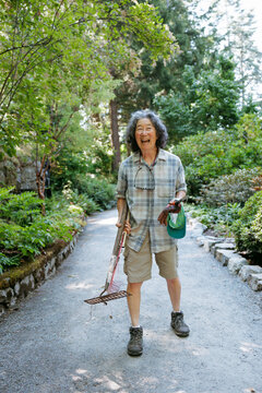 Smiling gardener holding tools in lush green outdoor garden
