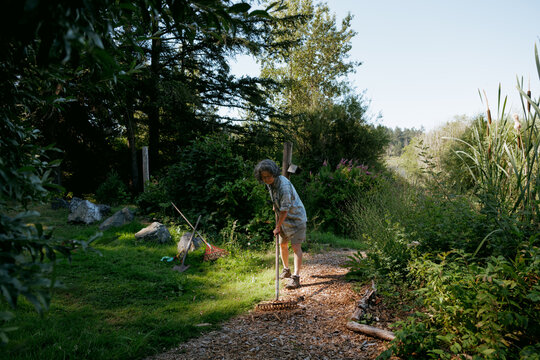 Person raking wood chips in a garden on a sunny day outdoors