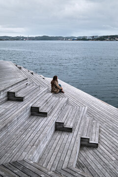Person Standing on Wooden Deck Overlooking Calm Ocean on a Cloudy Day