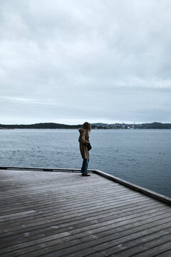 Person Standing on Wooden Deck Overlooking Calm Ocean on a Cloudy Day