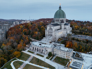 Aerial view of Saint Joseph Oratory in Montreal during autumn with colorful trees and city skyline at dusk. g.
