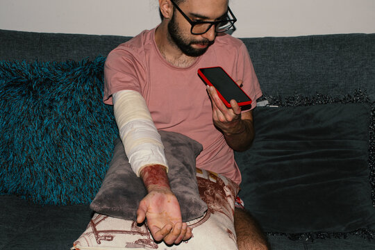 Man with bandaged arm sitting on couch and using phone