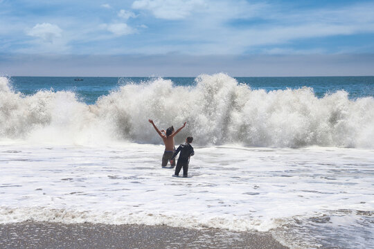 Teens stand in the ocean in front of large waves