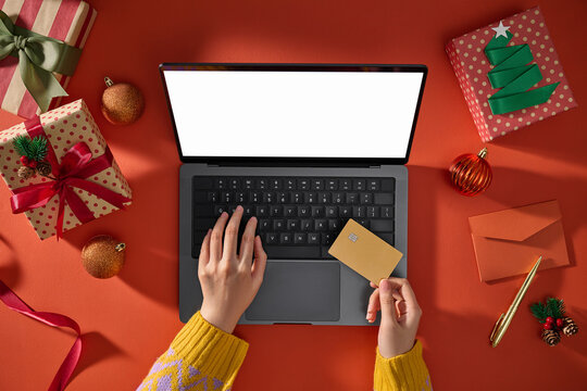 Hands hold a credit card near a laptop with gifts on red background