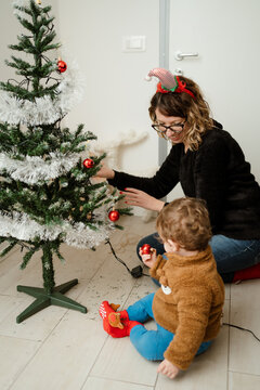 A baby decorating a Christmas tree at home with his mom