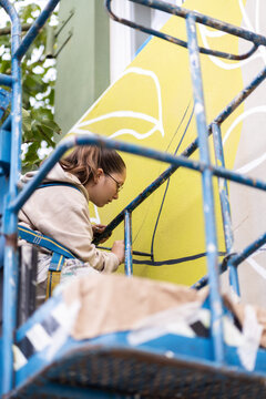 Female artist painting a mural on a building wall using a crane