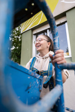 Smiling painter woman standing on aerial work platform is painting