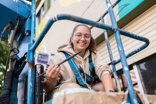 Smiling muralist painting a wall using a lift, street art creation