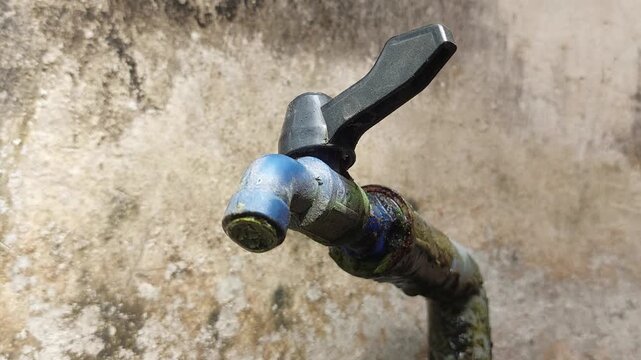 Close up cinematic video of an old outdoor water faucet covered in dirt and moss, mounted beside a house with a worn and weathered wall in the background. 