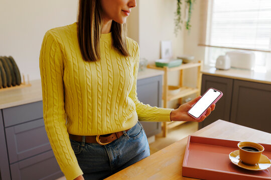 Woman using smartphone with blank screen in kitchen