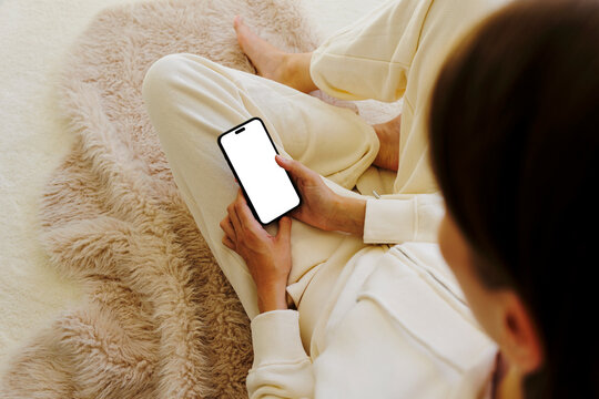 Woman relaxing on carpet using smartphone with blank screen