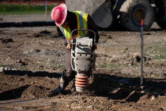 Construction worker using a compactor rammer machine to manually pack the fresh dirt covering trench a newly installed water pipeline, new municipal water distribution utility project work

