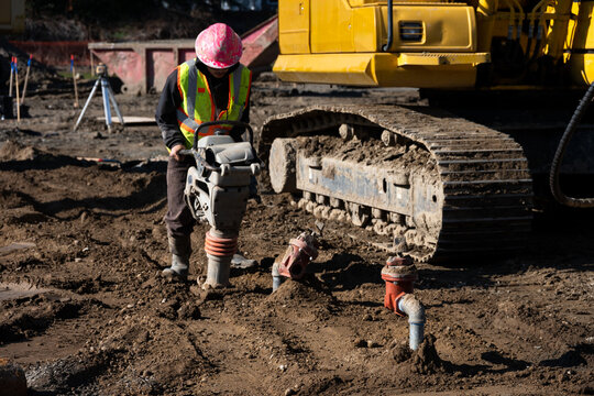 Construction worker using a compactor rammer machine to manually pack the fresh dirt covering trench a newly installed water pipeline, new municipal water distribution utility project work
