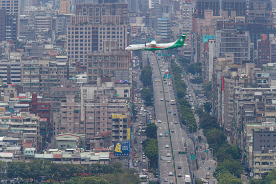 Taipei, Taiwan - 2018 April 18: A UNI Air ATR 72 aircraft flying low over a dense cityscape and an elevated highway on approach to land at Taipei Songshan Airport.