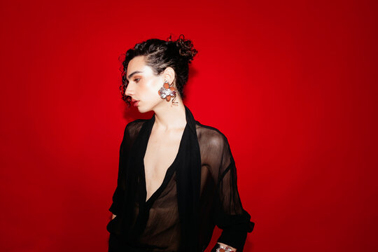 Queer man posing in sheer shirt fashion on red background