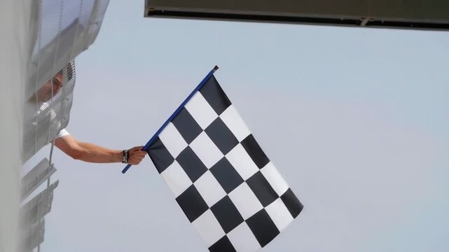 Person holding checkered flag in racing event with clear blue sky