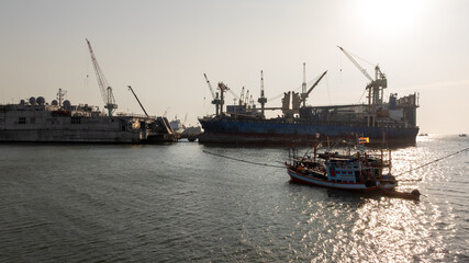 Obraz premium Traditional wooden Thai fishing boat with massive industrial and cargo terminal, Contrast and coexistence between local livelihoods and growth modern heavy industry.