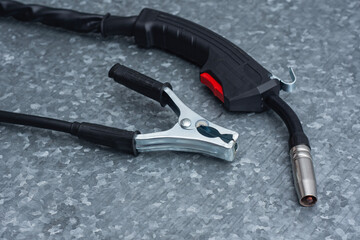 Welding torch and grounding clamp on a galvanized metal background. Industrial welding tools concept with professional equipment for MIG and TIG welding processes.