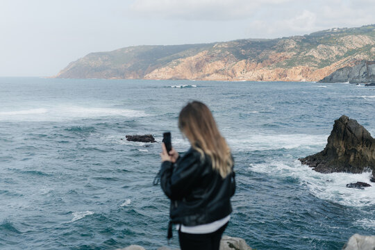 Young woman taking photos of the foaming Atlantic Ocean in Portugal