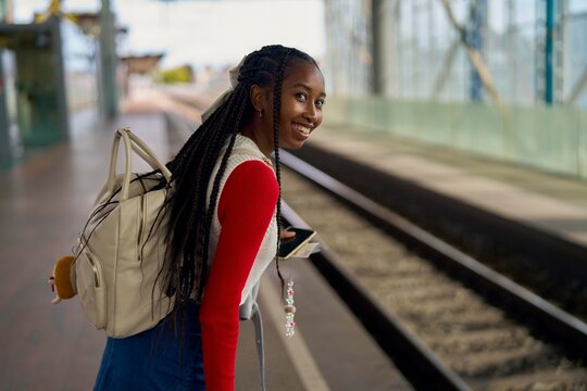 Joyful Girl Waiting at Train Station During Sunny Afternoon