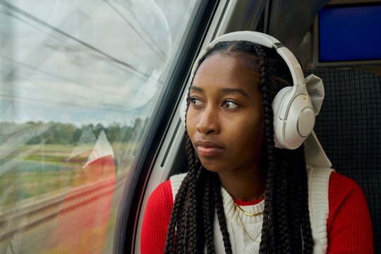 Young Woman Listening to Music and Looking out the Train Window