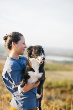A smiling woman is holding her mixed-breed dog in her arms