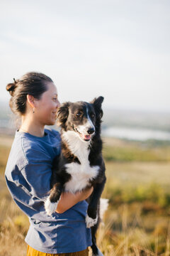 A smiling woman is holding her mixed-breed dog in her arms