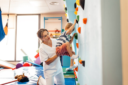 Physiotherapist assisting child climbing wall in therapy clinic