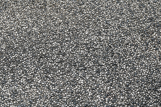A pebble wash or aggregate finish surface. Composed of a dense arrangement of small, rounded stones in a mix of colors. Used for outdoor flooring, pool decks, and architectural pathways.