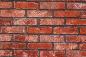 Obraz premium A full-frame background of a red brick wall, showcasing the rough, porous texture of the bricks and the contrasting black mortar.