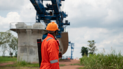 The survey team is operating a theodolite while referencing road construction plans. Civil engineers are taking measurements with surveying equipment at the construction site.
