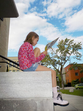 A young girl is reading a magazine sitting on a stone step in front of