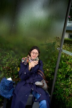 Busy City Dweller Checking Phone at Bus Stop on a Rainy Day