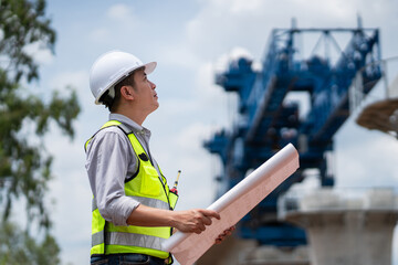 The survey team is operating a theodolite while referencing road construction plans. Civil engineers are taking measurements with surveying equipment at the construction site.