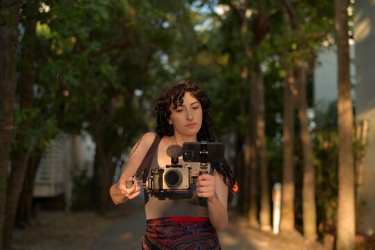 Young Woman Filming in a Wooded Environment During Golden Hour
